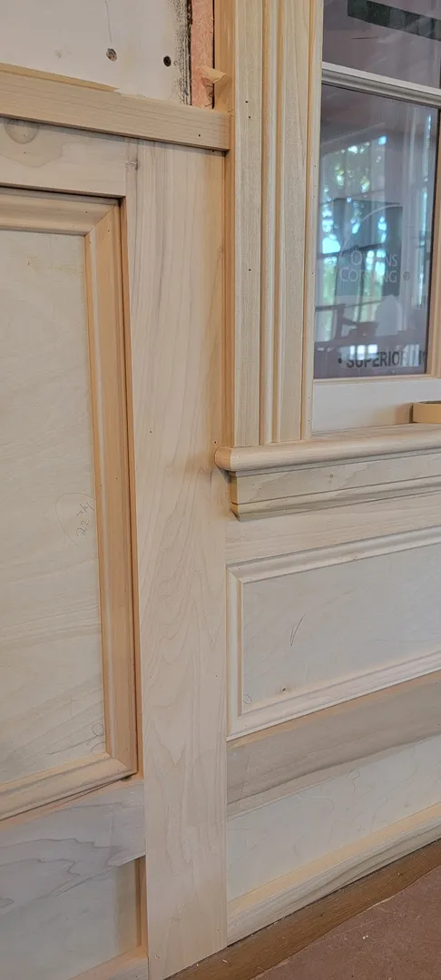 Close view of custom paneling, casing, and sill joinery around a window.