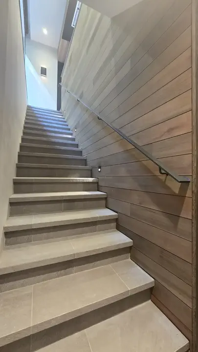 Stone stair rising beside a long wall of precisely aligned horizontal wood cladding and a black steel handrail.