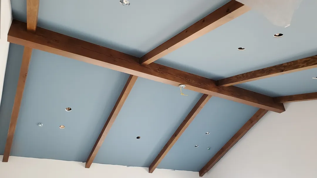 Finished timber beams dividing blue ceiling panels with coordinated lighting openings.