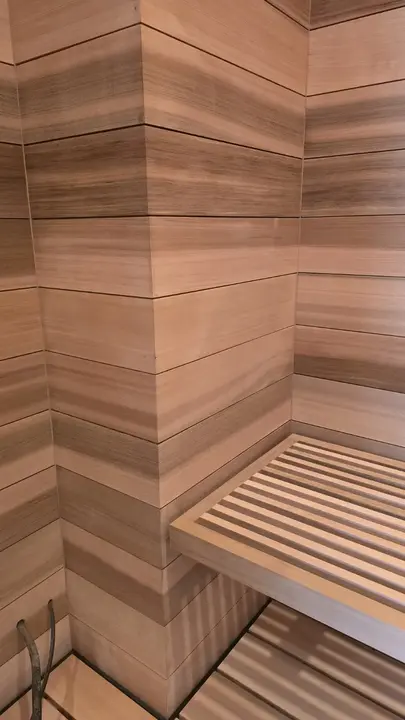 Close view of aligned cedar wall boards wrapping a sauna corner above a slatted bench.