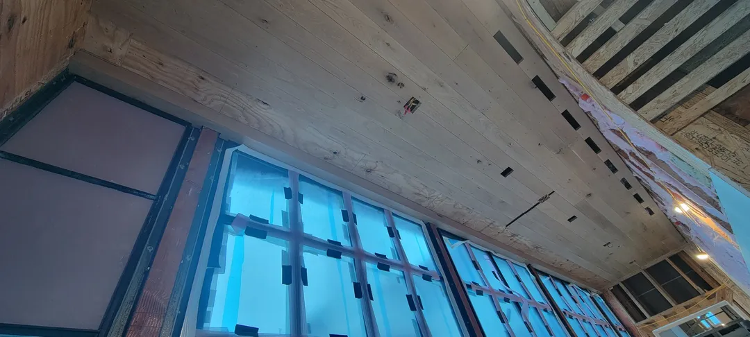 Long view of continuous wood ceiling paneling installed above a wall of tall windows.