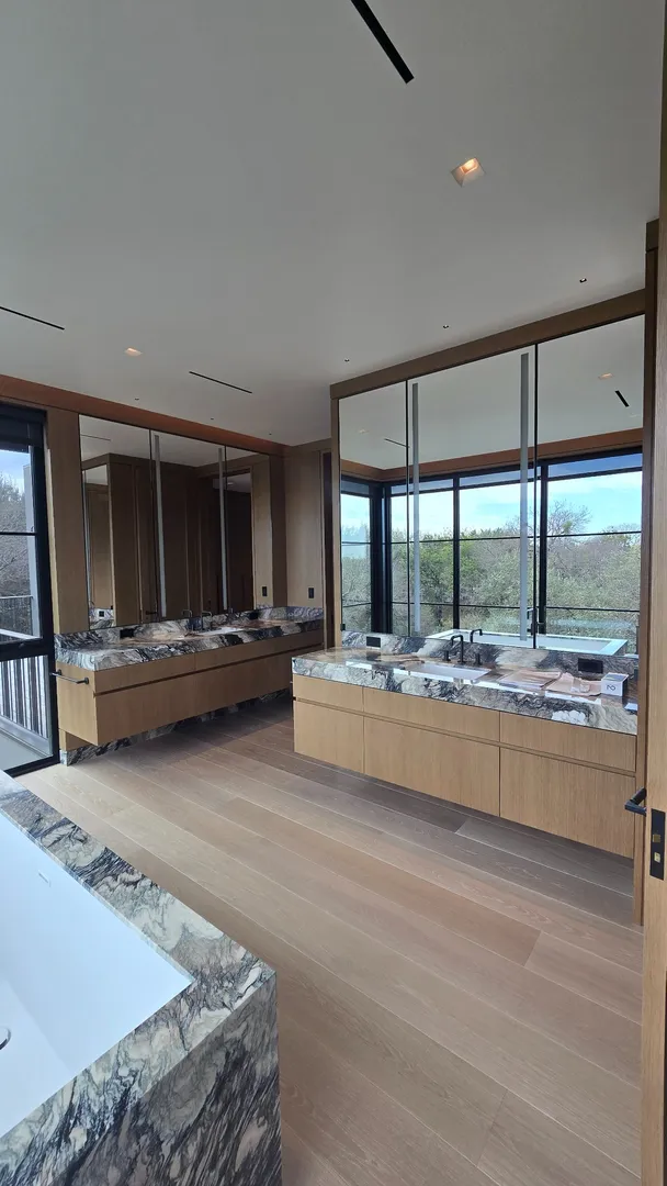 Installed white oak bathroom cabinetry, mirrored panels, and stone detailing at Las Lomas.