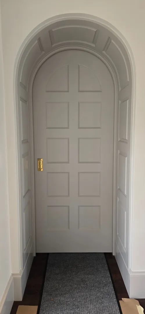 Tall white paneled arched door with polished brass hardware.