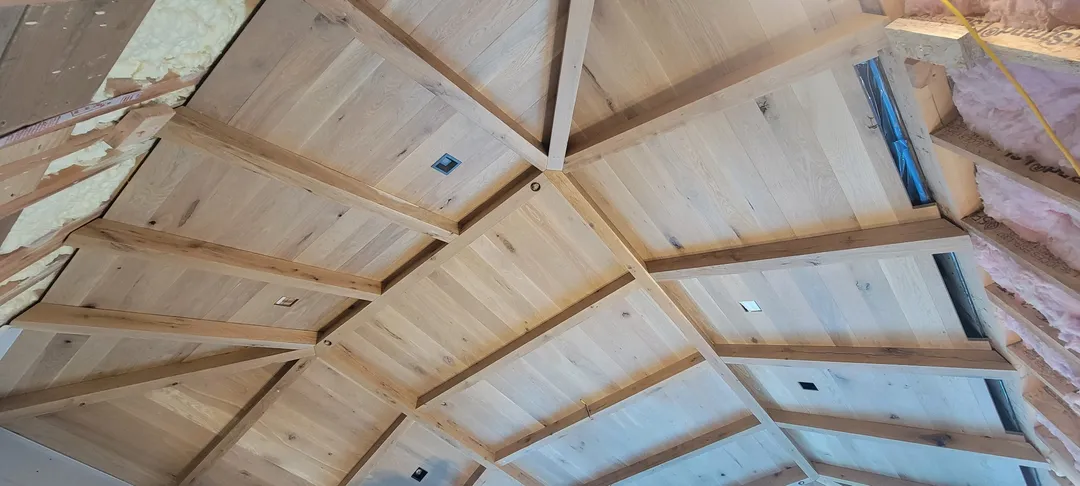 Close view of intersecting beams and fitted wood ceiling panels at a complex transition.