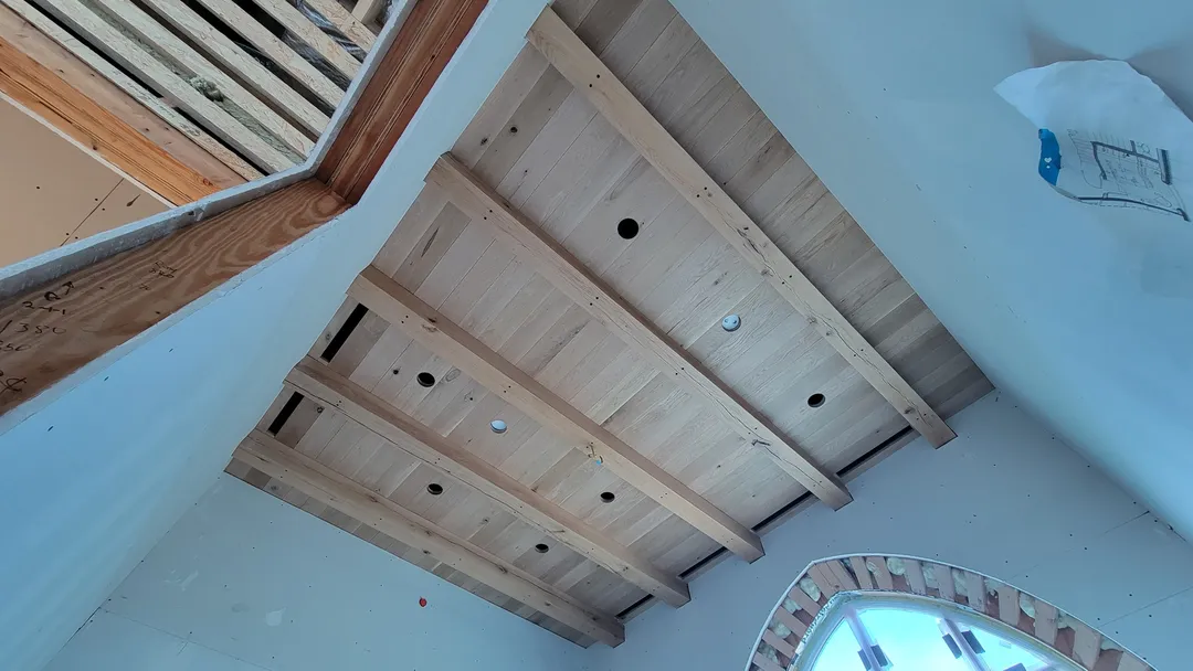 Wide room view showing the custom beam-and-panel ceiling installation above arched openings.