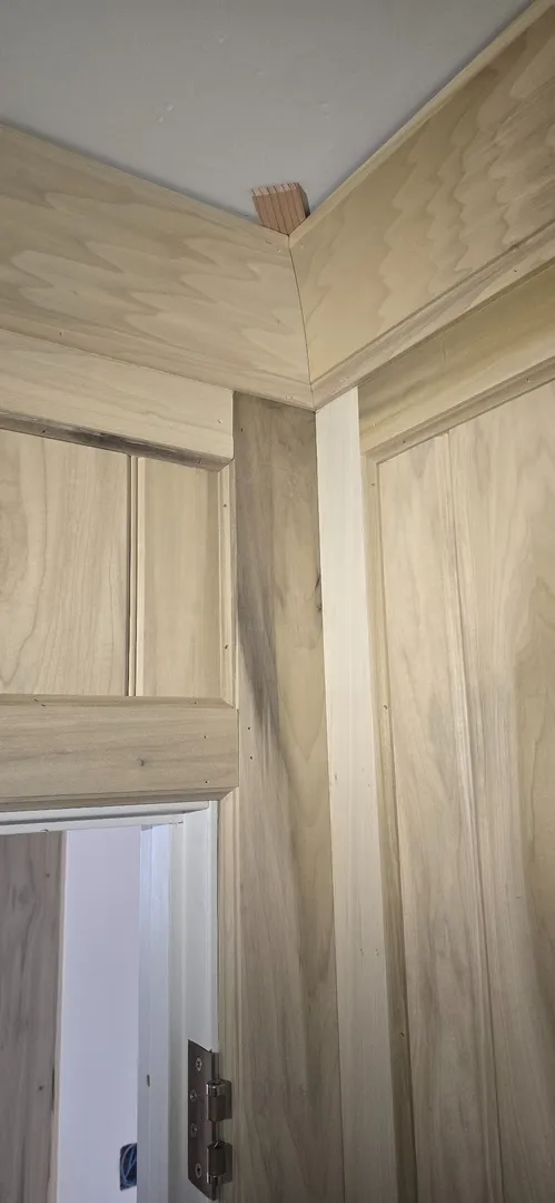 Mitered white oak casing and panel joints at a ceiling transition.