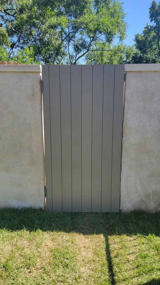 Custom vertical-panel garden gate centered between stucco walls.
