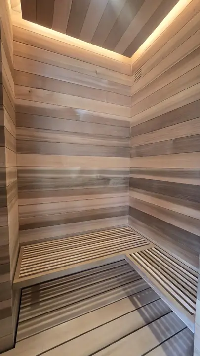 Custom cedar sauna interior with horizontal wall boards, slatted benches, and concealed perimeter lighting.