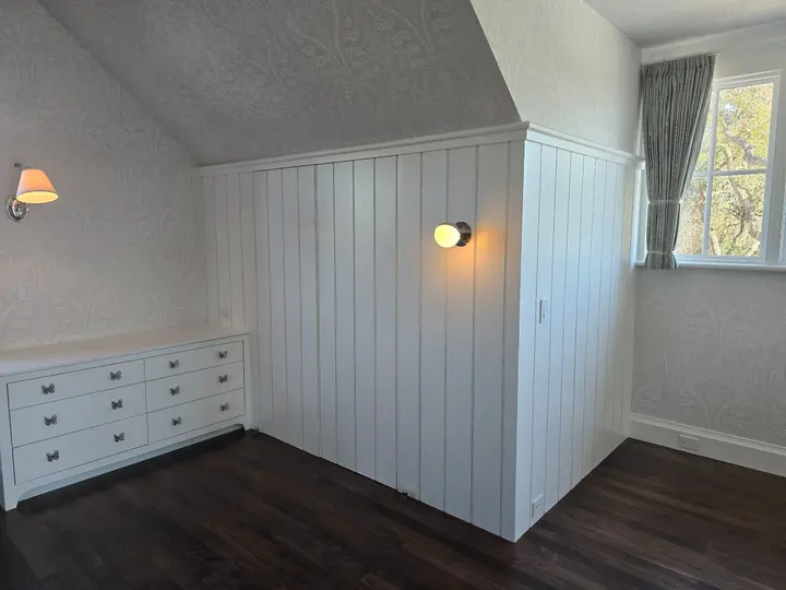 Wide view of a painted paneled bedroom enclosure, casework installation, wallpaper, and window detailing at Stoneridge.