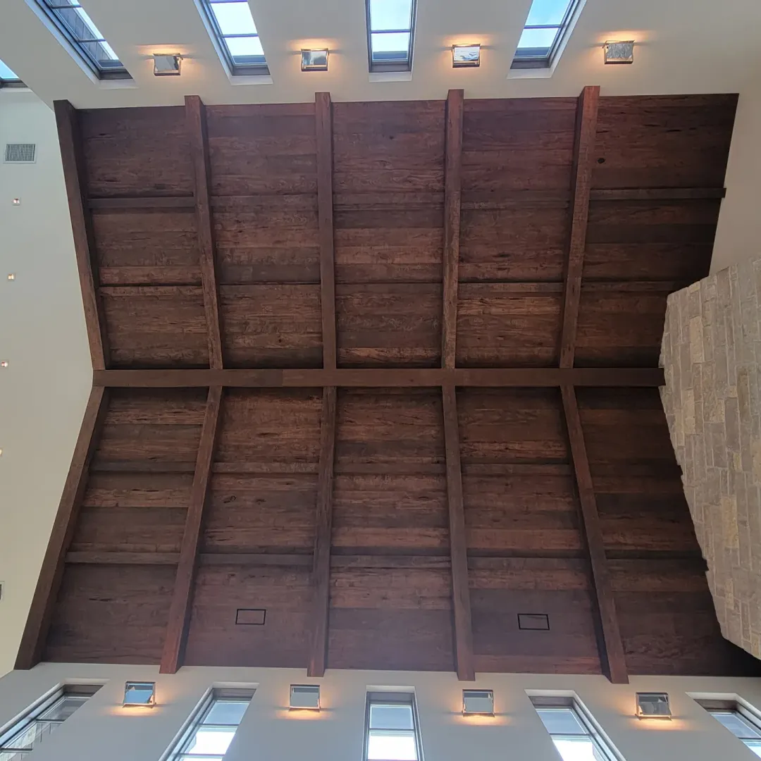 Centered view along the ridge of a completed vaulted wood ceiling with skylights and recessed lighting.
