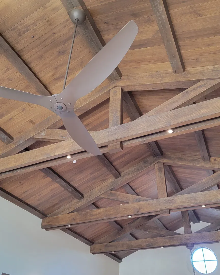 Exposed timber trusses, wood ceiling panels, and a large ceiling fan in the completed room.