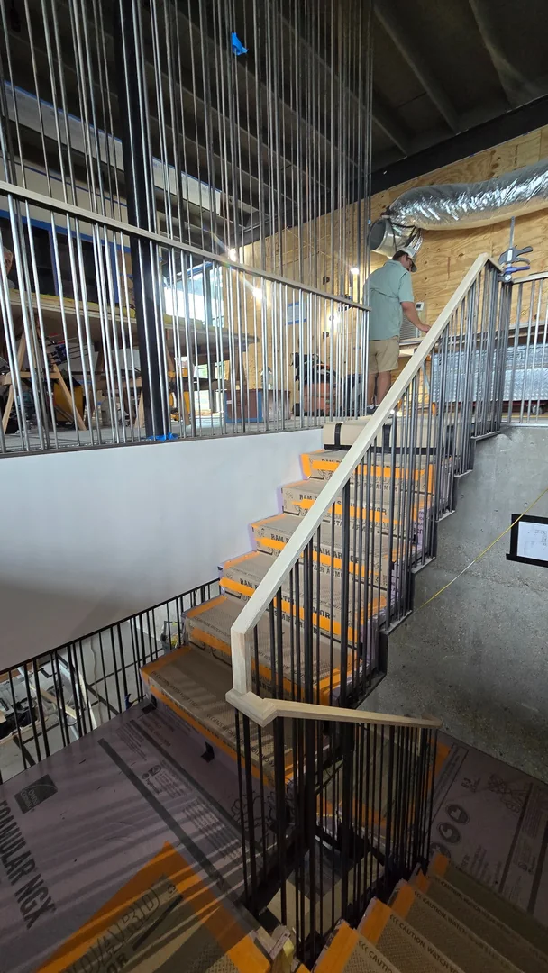 Staircase with wood handrails, metal balusters and a tall metal screen during construction.